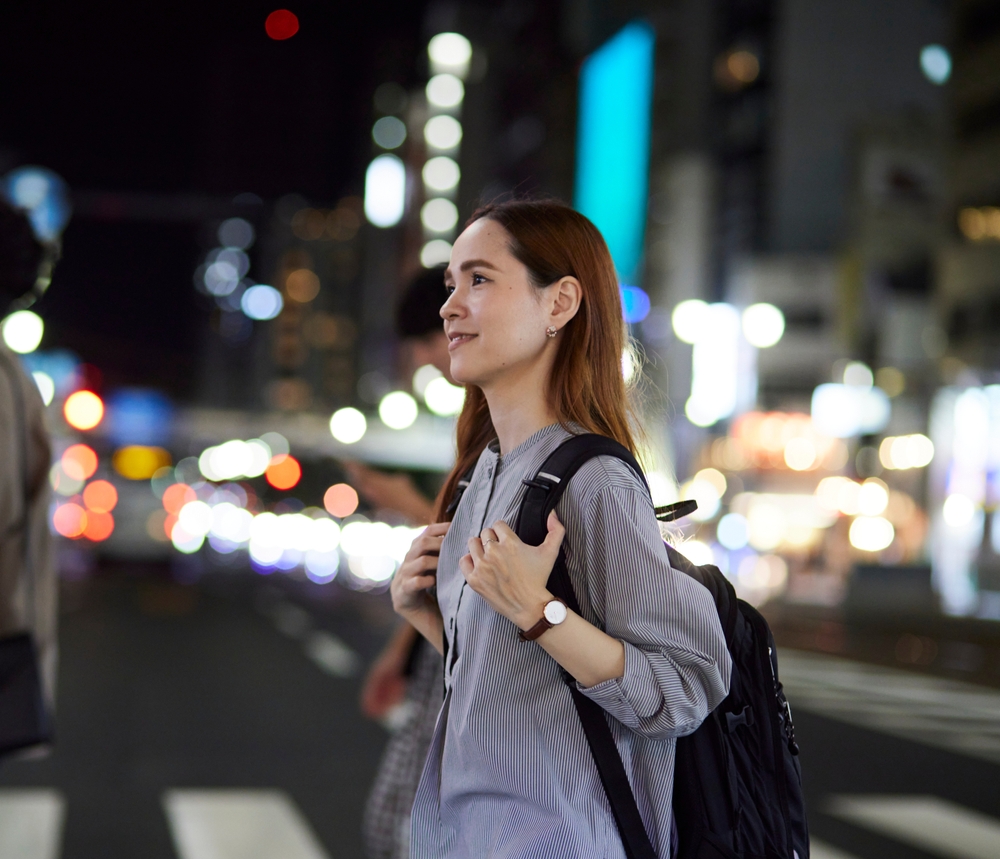 リュックを背負い、夜の街を笑顔で歩く女性
