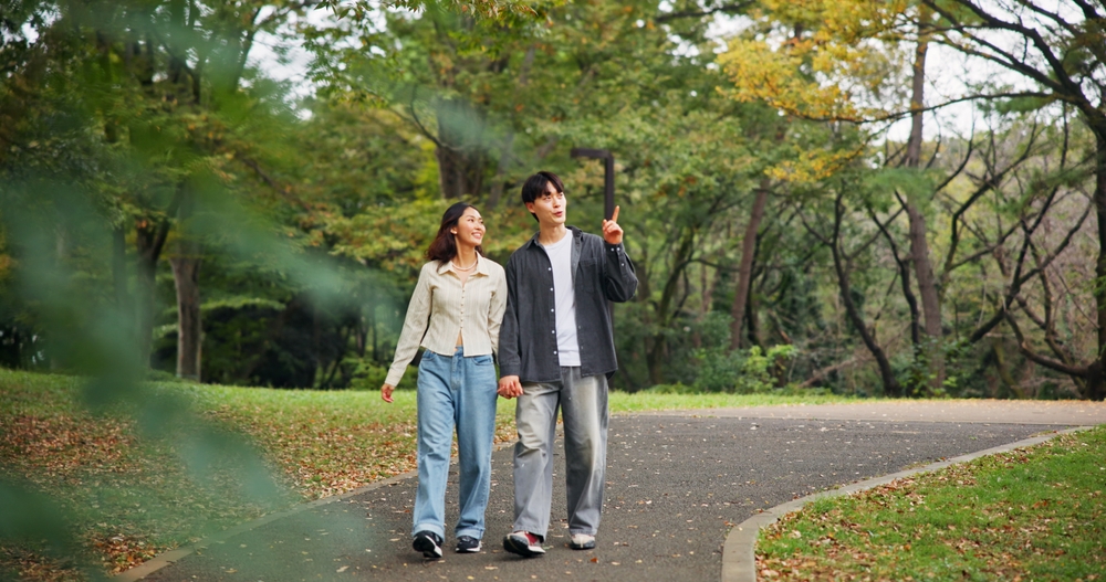 緑豊かな公園の遊歩道を、笑顔で並んで歩いている若い男女の様子