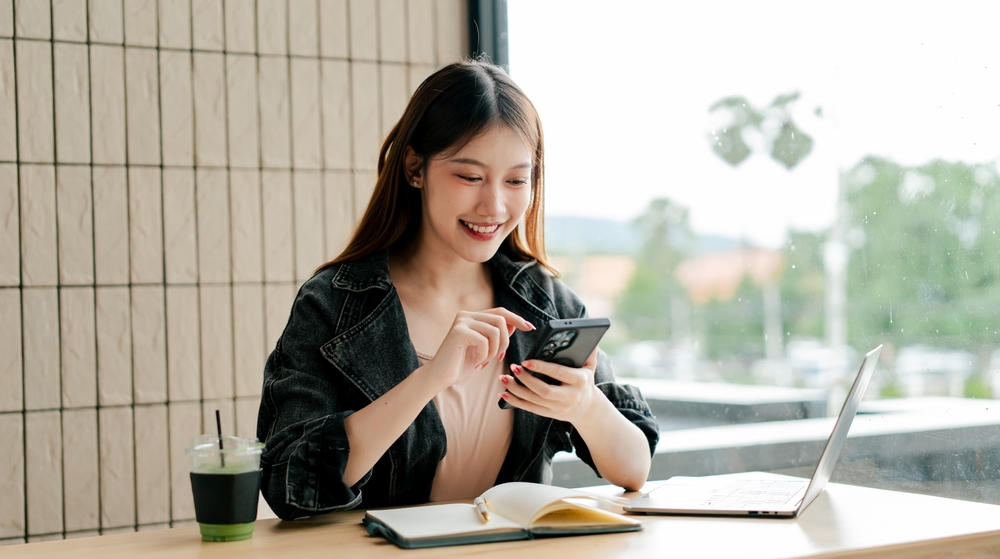カフェでスマートフォンを笑顔で操作する女性