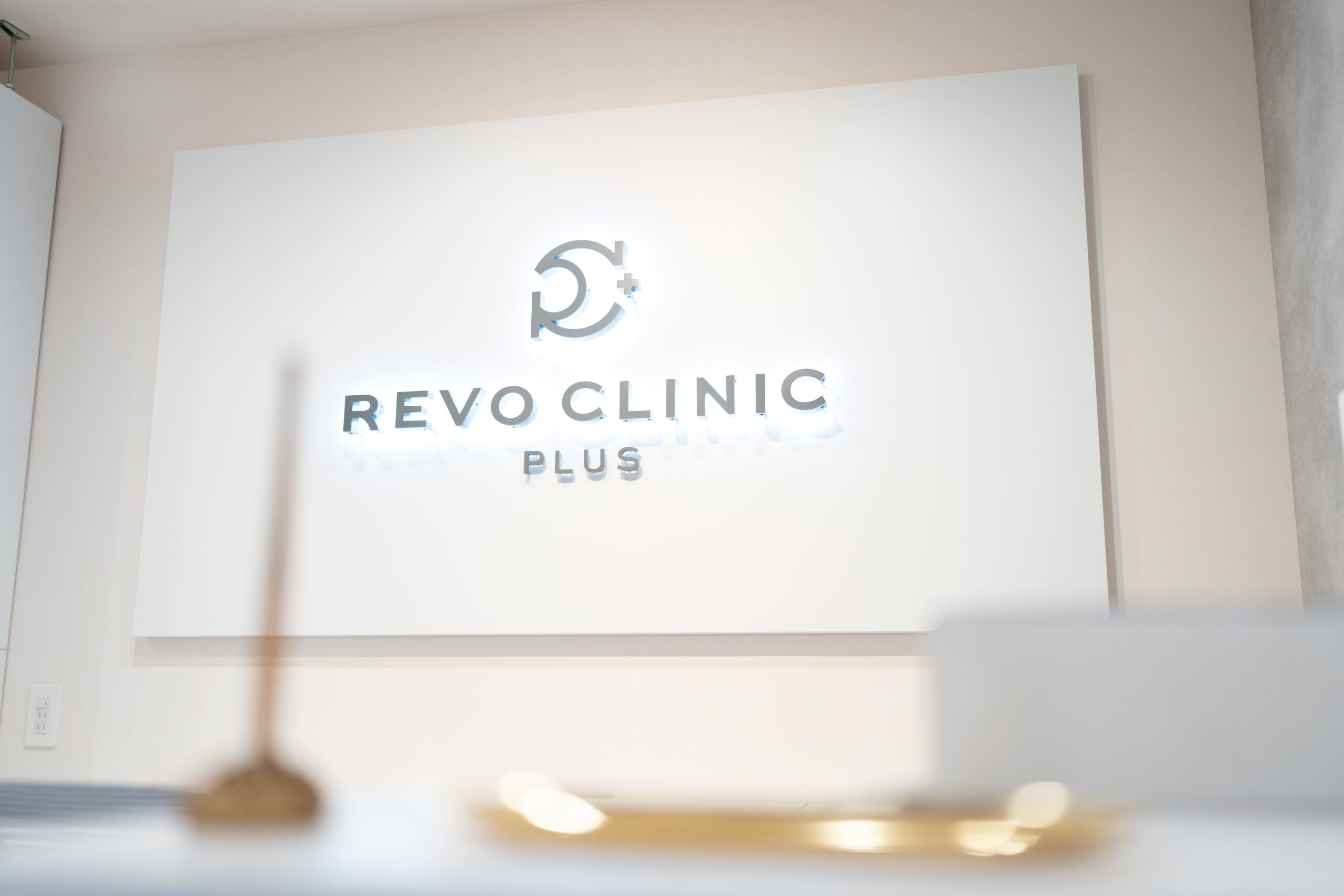 受付の白い壁に掲げられたREVO CLINIC PLUSのロゴ