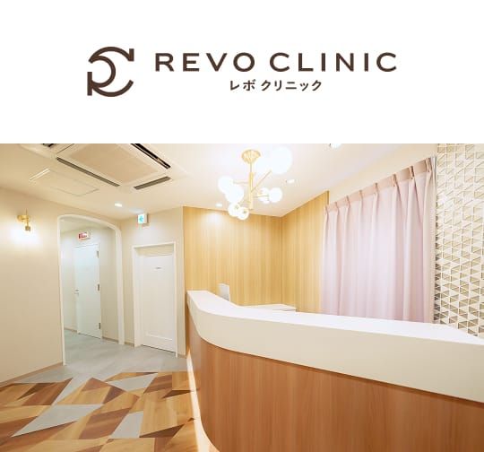 REVO CLINICのロゴと、木目調のフロントカウンターがある清潔感のある受付内観